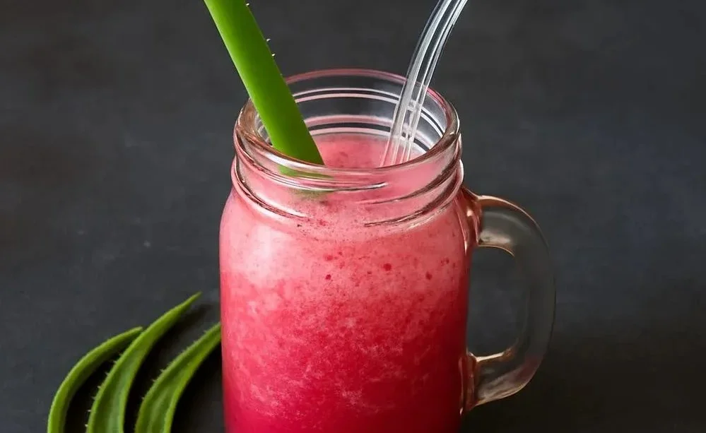 Aloe vera smoothie in a glass garnished with fresh fruits and mint leaves.