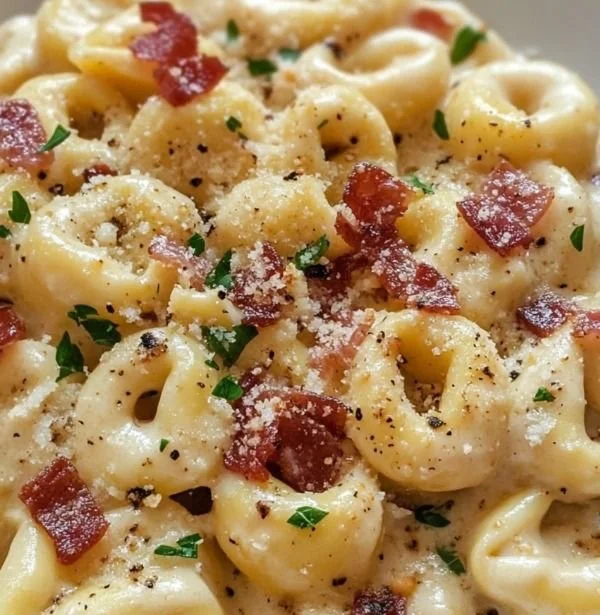 A bowl of Tortellini Carbonara garnished with parsley and cheese.
